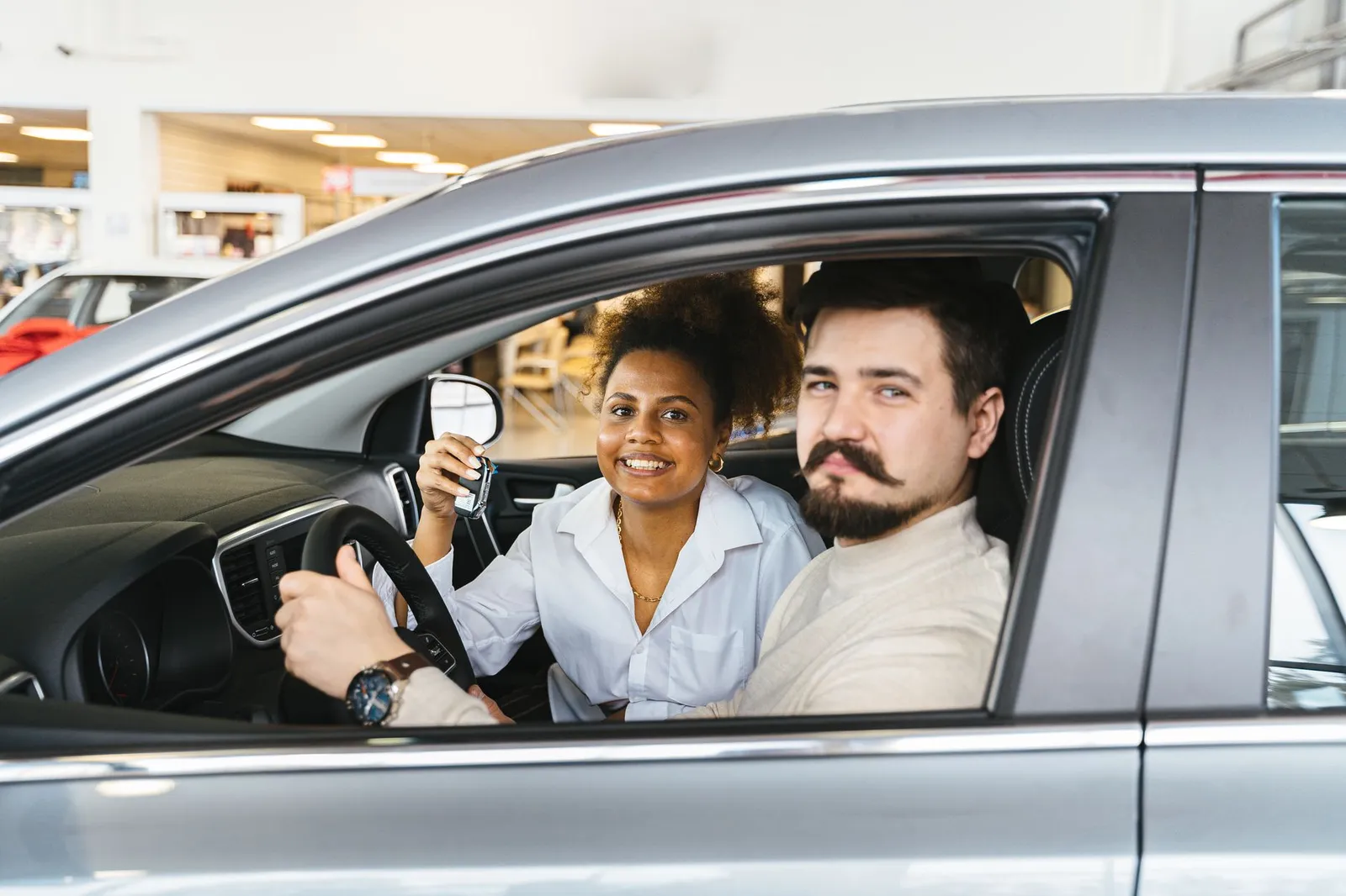 A smiling couple holding the key inside their new car