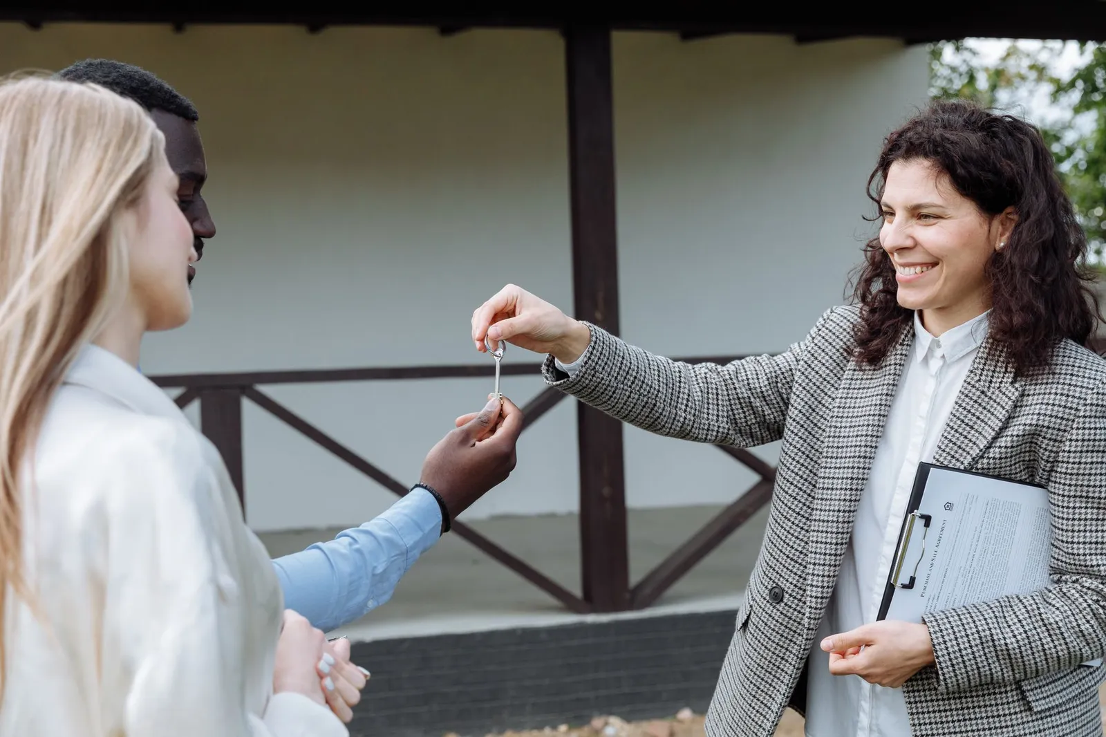 An agent handing house keys to a smiling couple outside their new home