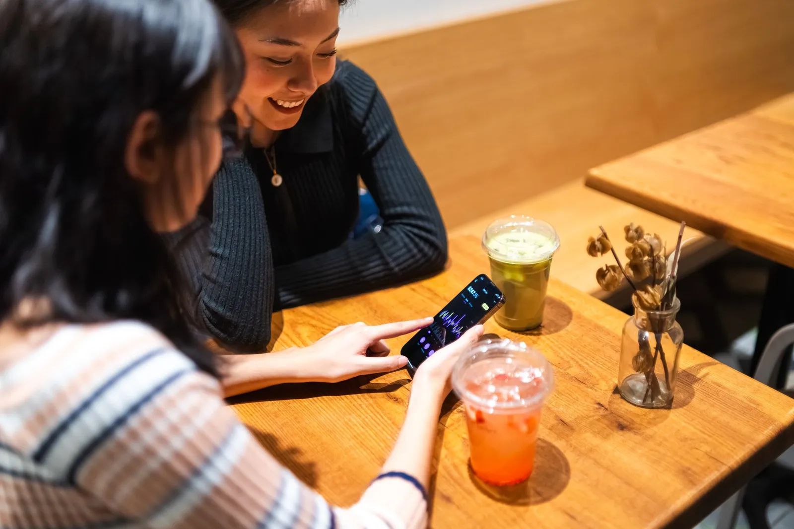 Two friends at a cafe checking a finance app on a phone